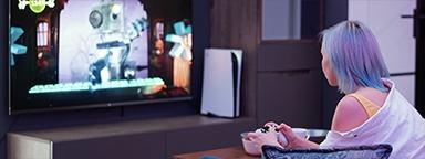 Девушка-геймер держит контроллер PS5, на заднем плане - видеоэкран